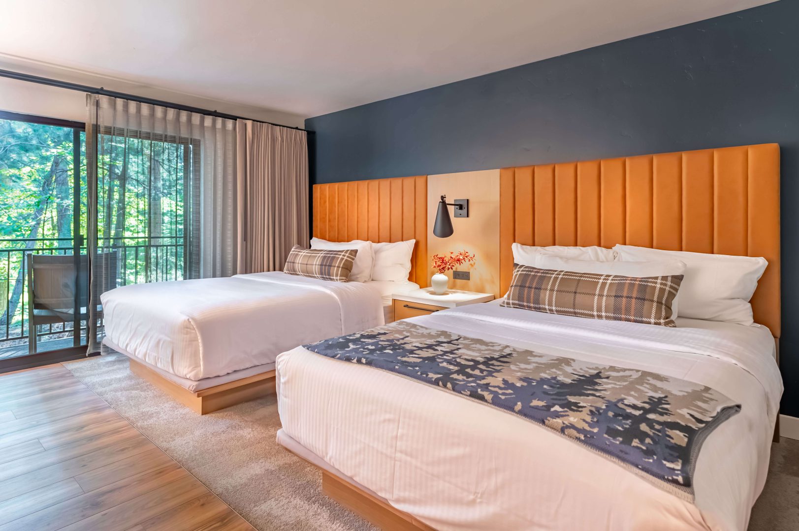 Two queen beds with white linens and pillows, light brown headboards and a balcony in the Alpine View room at The Incline Lodge.