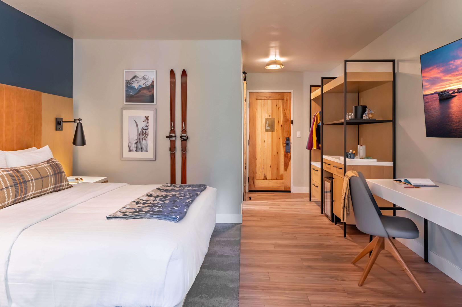 A king bed with white linens and pillows, a wardrobe, and a white desk in a spacious room at The Incline Lodge.