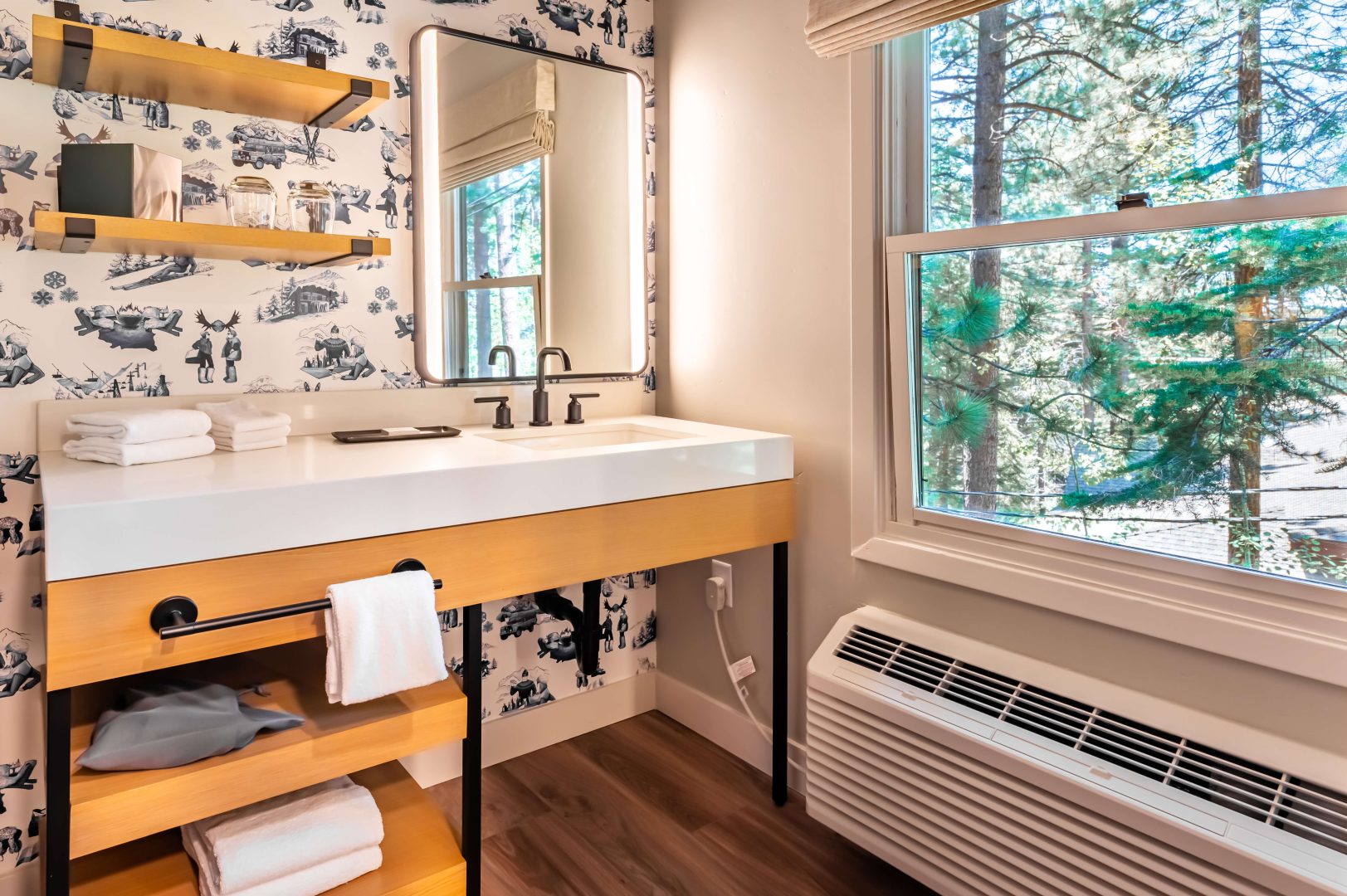 A large white vanity, a lit mirror, a window, and a heater, in a bathroom at The Incline Lodge.